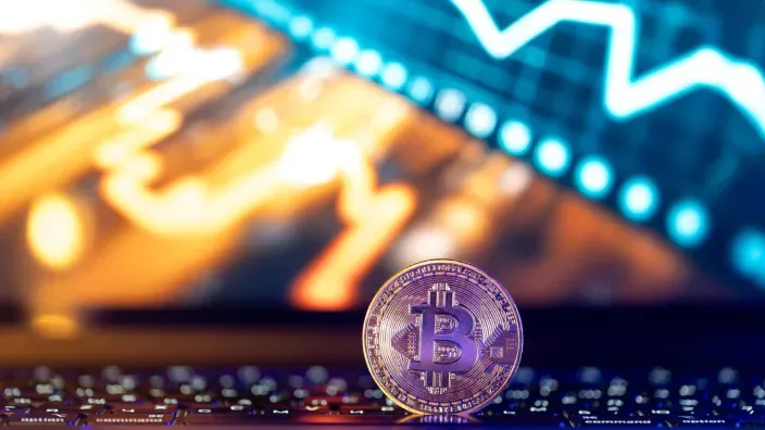 Bitcoin sobre un teclado con un gráfico de cotización desenfocado al fondo