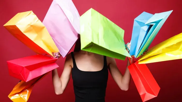 Mujer oculta tras bolsas de compras de colores sosteniendo una tarjeta de crédito roja.