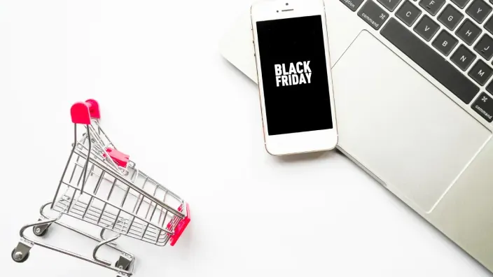 Concepto compras Black Friday online con carrito de supermercado miniatura y smartphone sobre escritorio.