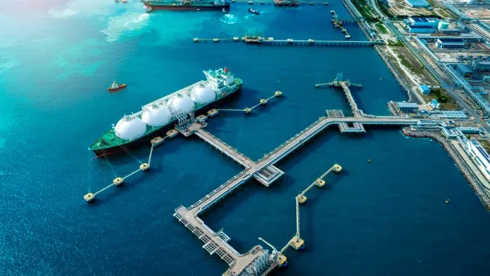 Buque metanero de transporte de gas natural licuado GNL atracado en terminal portuaria.