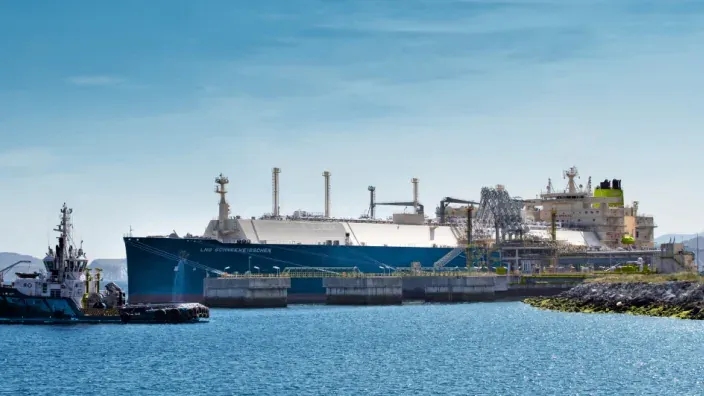 Buque metanero atracado en una terminal portuaria de gas natural licuado (GNL) durante operaciones de carga y descarga.