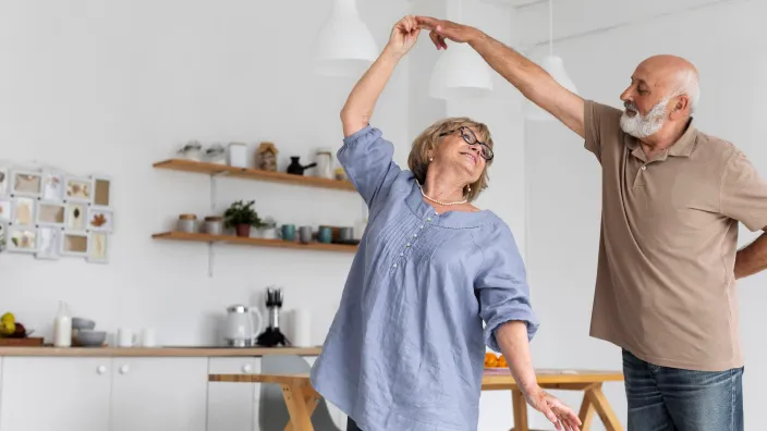 Pareja de jubilados felices bailando en la cocina de su casa, disfrutando de una jubilación activa y tranquila.