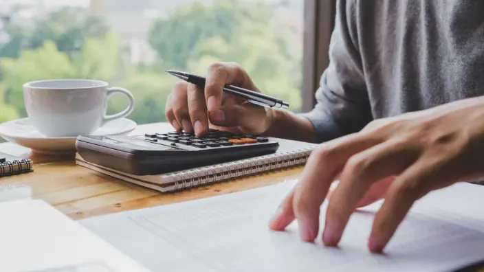 Persona usando una calculadora y revisando documentos de gastos en casa.