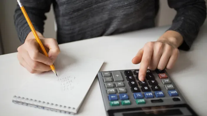 Persona usando una calculadora y tomando notas para realizar el cálculo de impuestos o la contabilidad del hogar.