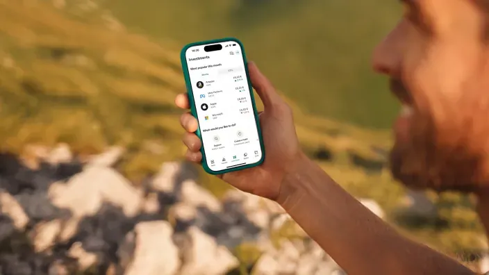 Hombre usando la app de inversiones de N26 en su móvil mientras hace senderismo en la naturaleza.