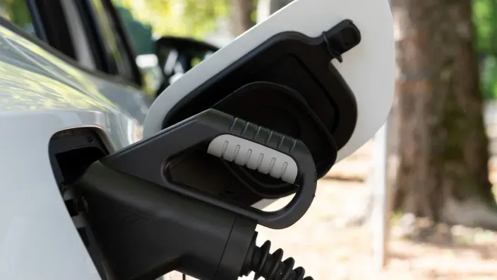 Primer plano de un enchufe de cargador eléctrico conectado al coche para que este cargue las baterías.