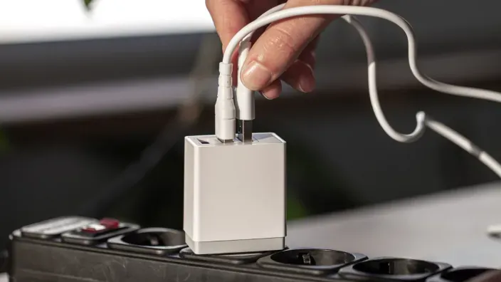 Mano desenchufando un cargador blanco de una regleta para reducir el consumo eléctrico.