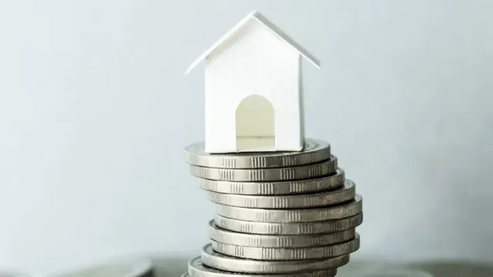 Casa en miniatura colocada sobre una pila de monedas simbolizando el ahorro para vivienda.