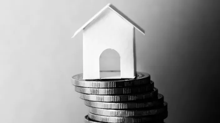 Figura de una casa colocada sobre una pila de monedas, en fotografía en blanco y negro.