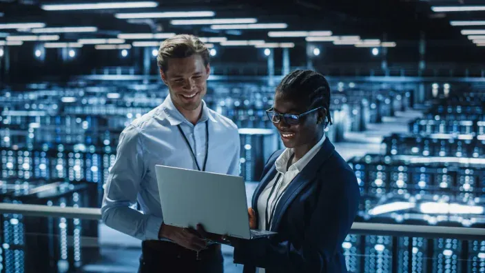 Dos ingenieros de TI colaborando en un centro de datos revisan la información del servidor en un portátil.