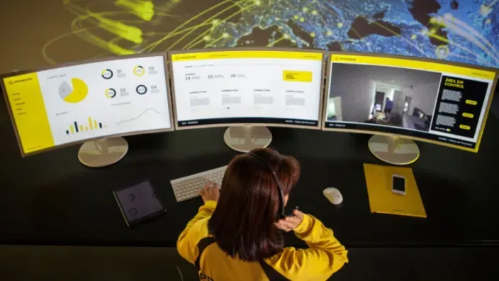 Operadora de seguridad monitoreando cámaras y datos en pantallas de una central de vigilancia.