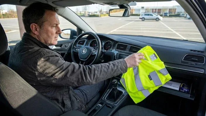 Conductor sacando el chaleco reflectante de seguridad de la guantera del coche antes de salir del vehículo.