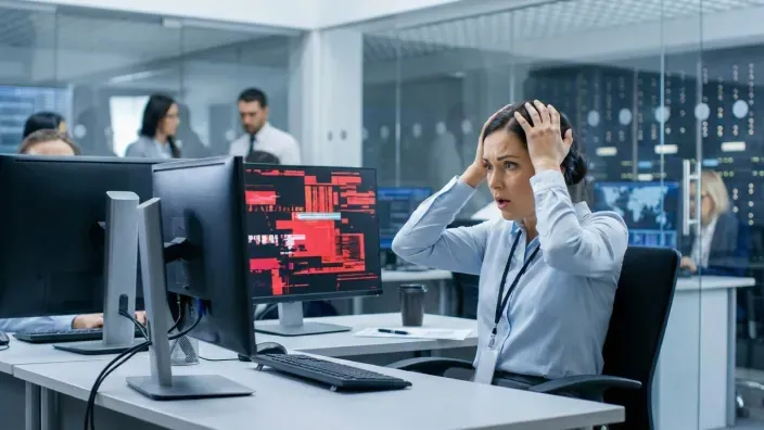 Mujer preocupada en una oficina ante un error de sistema en su pantalla como concepto de ciberataque y falta de seguridad.