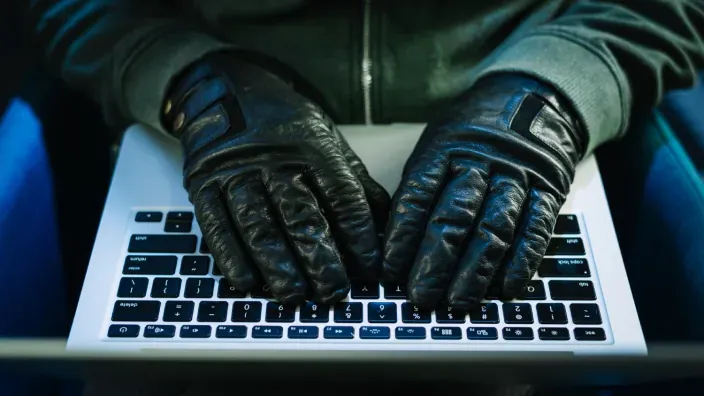 Hacker con guantes negros tecleando en un ordenador portátil como concepto de ciberdelincuencia y falta de seguridad informática.