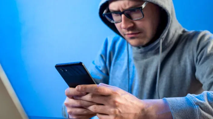 Hacker con capucha y gafas usa su móvil para una estafa.