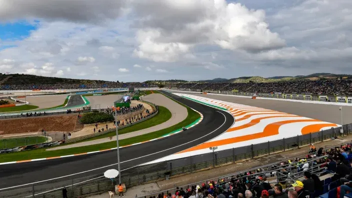 Vista panorámica del circuito Ricardo Tormo de Valencia durante una carrera de MotoGP, con gradas llenas de aficionados y curvas decoradas en naranja y blanco.