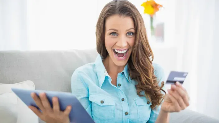Mujer emocionada con tablet y tarjeta de crédito en el sofá de su casa.
