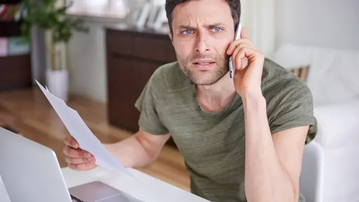 Hombre preocupado hablando por teléfono y revisando una factura Jazztel en su portátil para realizar una reclamación.