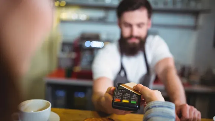 Cliente realizando un pago con tarjeta en un datáfono atendido por un camarero.