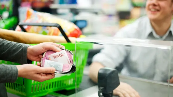 Cliente pagando en efectivo con billetes de euro en la caja del supermercado ante el cajero.