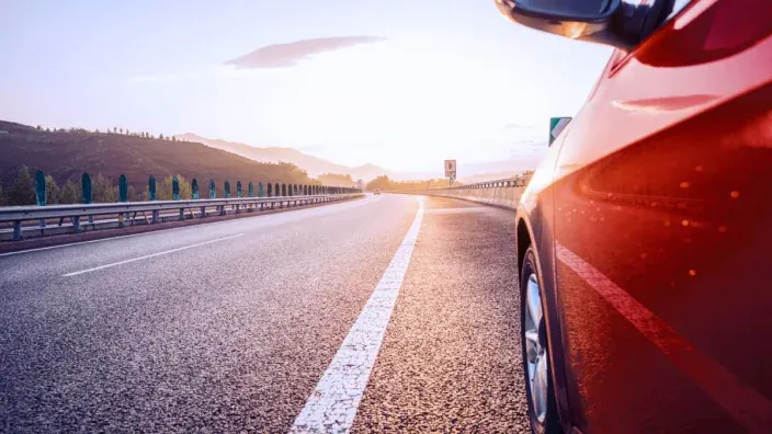 Coche en el arcén de una carretera al atardecer con montañas de fondo.