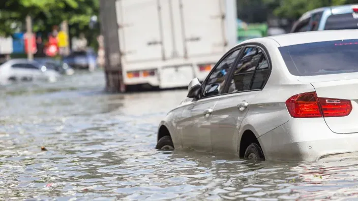 Coche blanco parcialmente sumergido en calle inundada tras lluvias torrenciales o riada.