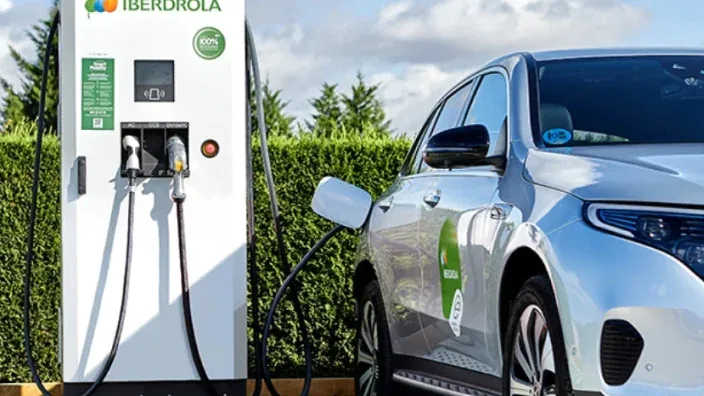 Hombre cargando un coche eléctrico rojo en un punto de recarga de Iberdrola en la vía pública.