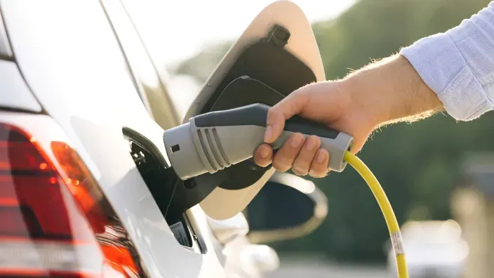 Persona conectando un coche eléctrico a un cargador doméstico.