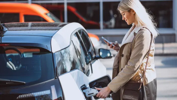 Mujer cargando su coche eléctrico mientras usa el móvil.