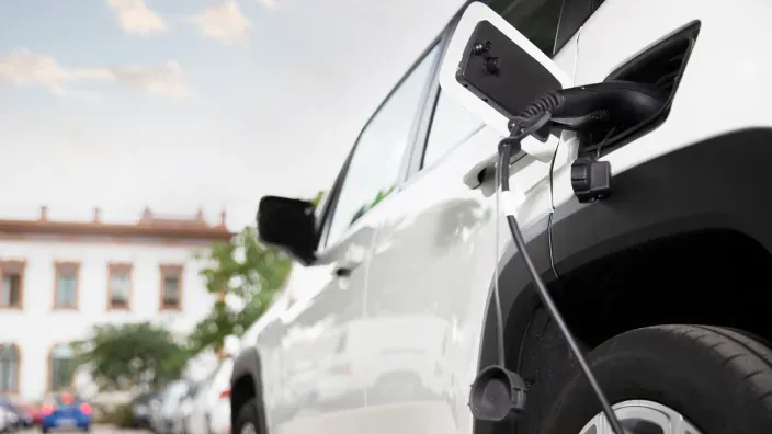 Coche eléctrico blanco conectado a un punto de recarga en una ciudad española.