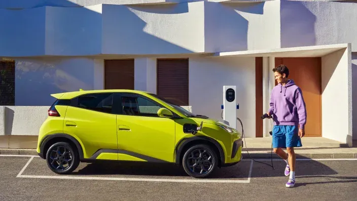 Joven cargando un coche eléctrico verde en un punto de recarga urbana.