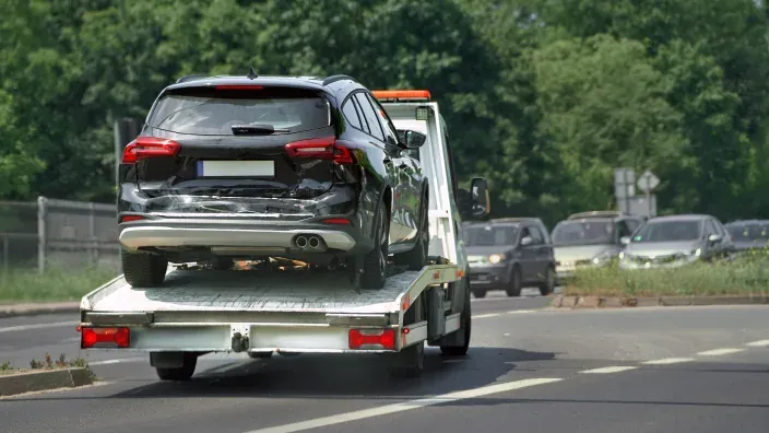 Grúa de asistencia en carretera remolcando un coche negro accidentado tras siniestro vial.