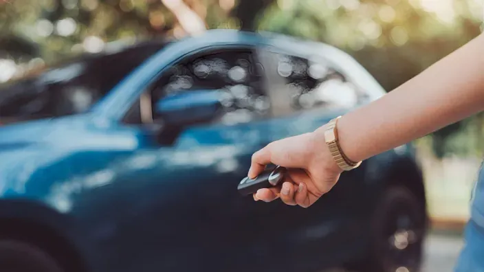 Mando a distancia desbloqueando un coche azul, representando el seguro de auto y la seguridad vial.