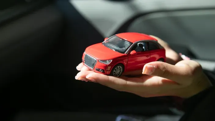 Manos sosteniendo un pequeño coche rojo de juguete para representar la protección y el seguro de automóvil.