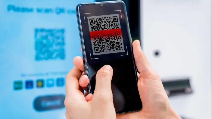 Mano sosteniendo un smartphone mientras escanea un código QR en una pantalla azul.