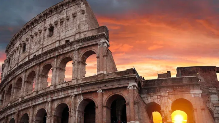 Coliseo de Roma iluminado por un atardecer con cielo anaranjado.