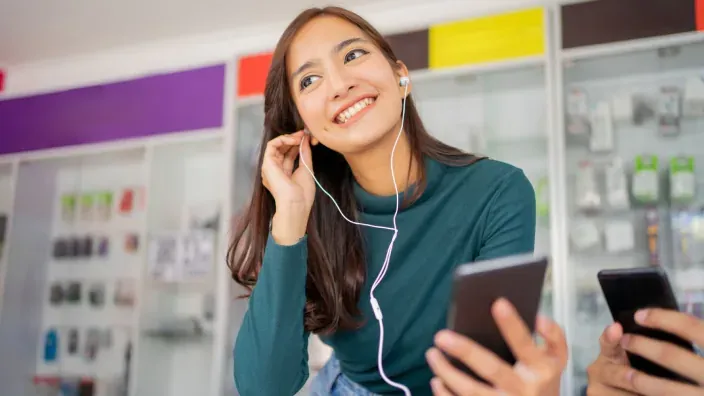 Clienta usando auriculares con cable y telefonía móvil en una tienda de tecnología.