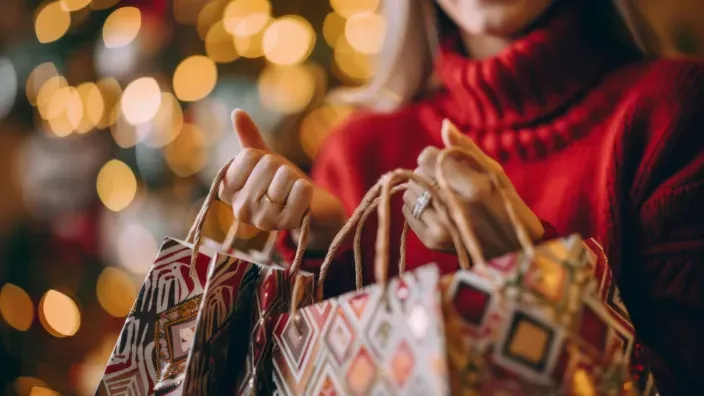 Mujer sosteniendo bolsas de regalo de Navidad con estampado geométrico y luces bokeh.