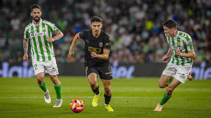 André Almeida, jugador del Valencia CF, controla el balón ante la mirada de dos defensores del Real Betis.