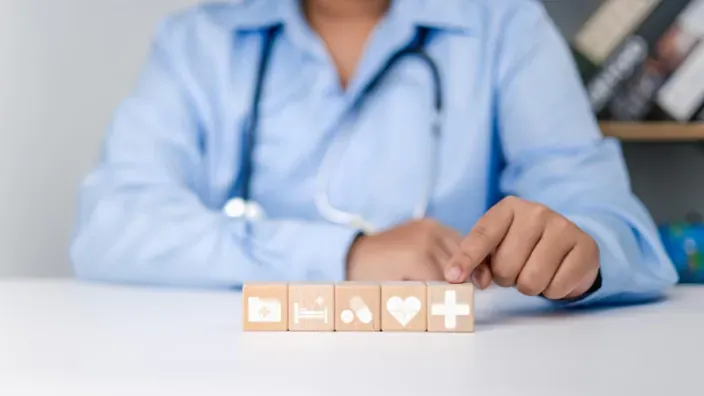 Doctora señalando cubos de madera con iconos de salud. Símbolo de seguro médico, hospitalización y asistencia sanitaria.