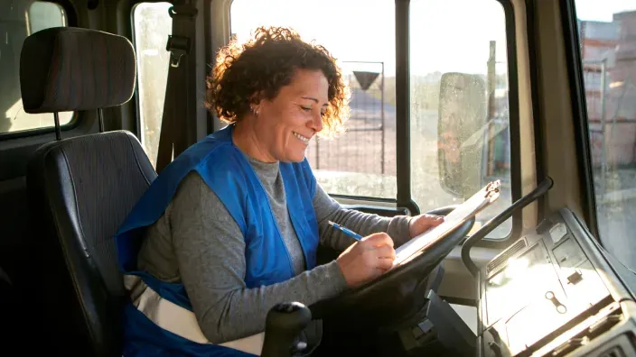 Mujer transportista profesional revisando su hoja de ruta en la cabina de un camión.