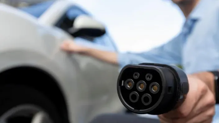 Conector de carga de coche eléctrico en primer plano junto a un coche