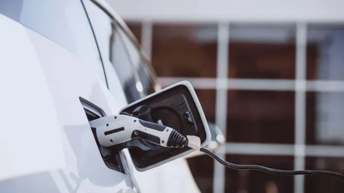 Conector de carga enchufado a un coche eléctrico blanco.