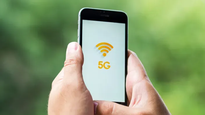 Persona sosteniendo un teléfono móvil con el icono de red 5G en pantalla, representando conectividad de alta velocidad.