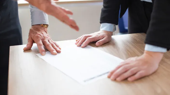 Disputa o negociación sobre un contrato de seguros o bancario entre dos personas en un escritorio de oficina.