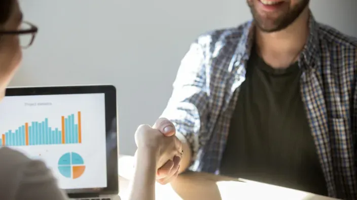 Apretón de manos profesional con gráficas de fondo para simbolizar un acuerdo de inversión.