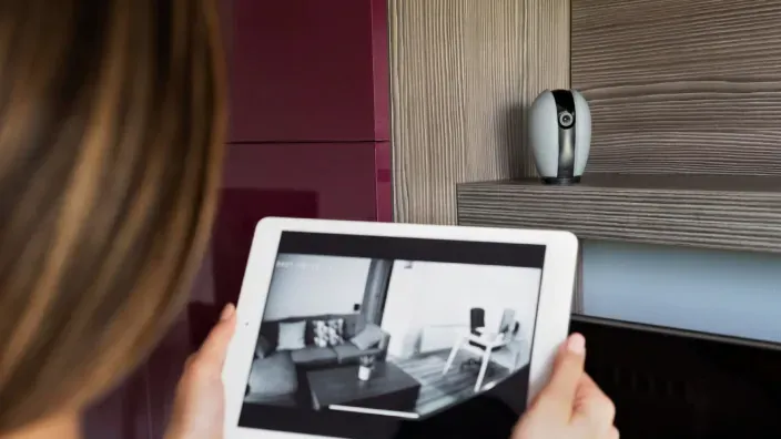 Mujer usando tablet para visualizar la señal de una cámara de seguridad inteligente en su salón.