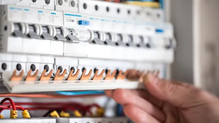 Cuadro eléctrico con interruptores automáticos y mano manipulando un peine de conexiones