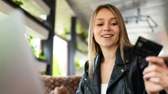 Mujer joven sonriente realizando compras online con su tarjeta de crédito desde un ordenador portátil.