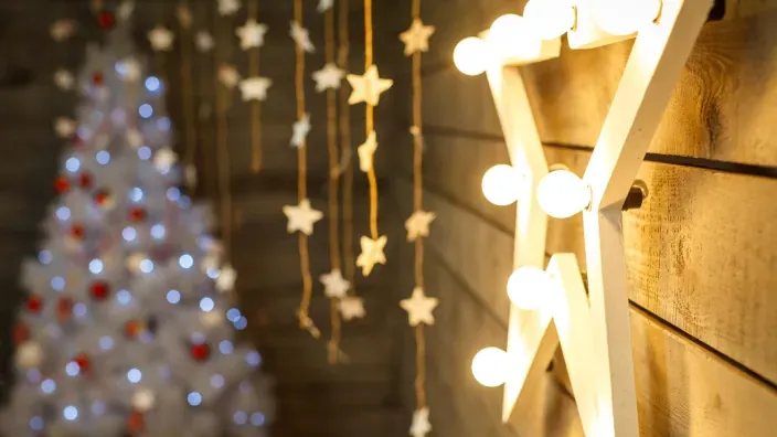 Estrella decorativa navideña iluminada con bombillas cálidas sobre fondo de madera y árbol.